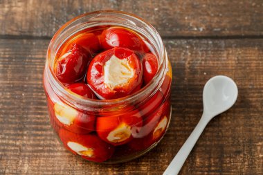 Doldurulmuş kiraz biberi ve ricotta peyniri ahşap arka planda cam kavanozu dolduruyor.