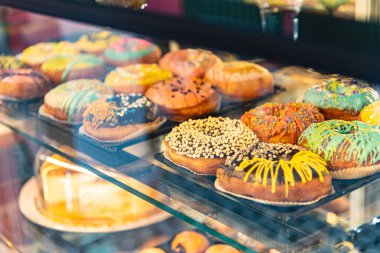 Kafe cam dolabında farklı dekorasyonlarla süslenmiş lezzetli çörekler. Seçici odak mavisi arkaplan