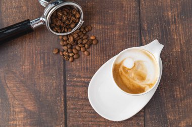 Kahveyi, beyaz porselen bardakta, ahşap masada rahatlatıyor.
