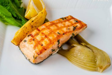 Beyaz porselen tabakta ızgara somon filetosu ve sebze karışımı.