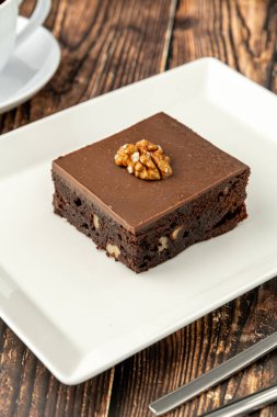 Ahşap masada beyaz bir porselen tabakta cevizli ve siyah çikolatalı brownie.