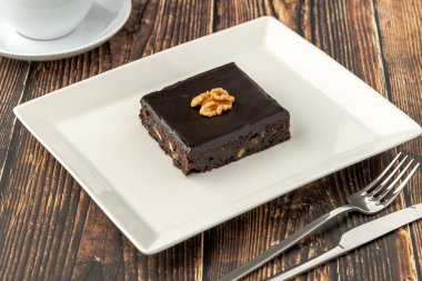 Ahşap masada beyaz bir porselen tabakta cevizli ve siyah çikolatalı brownie.