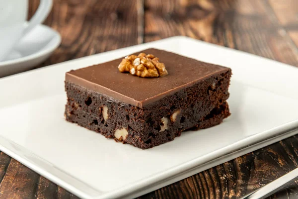 Ahşap masada beyaz bir porselen tabakta cevizli ve siyah çikolatalı brownie.
