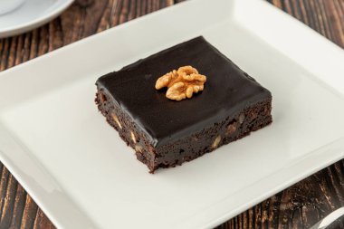 Ahşap masada beyaz bir porselen tabakta cevizli ve siyah çikolatalı brownie.