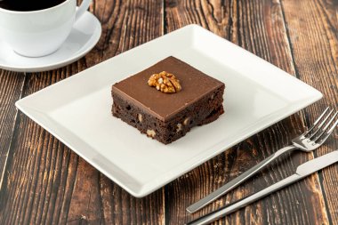 Ahşap masada beyaz bir porselen tabakta cevizli ve siyah çikolatalı brownie.