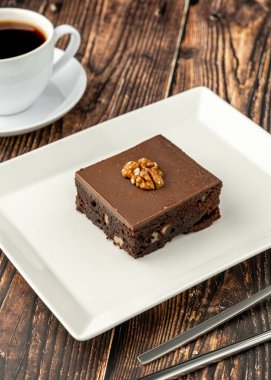 Ahşap masada beyaz bir porselen tabakta cevizli ve siyah çikolatalı brownie.