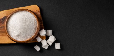 Tahta kasede koyu arkaplanda granüle şeker ve şeker küpleri.