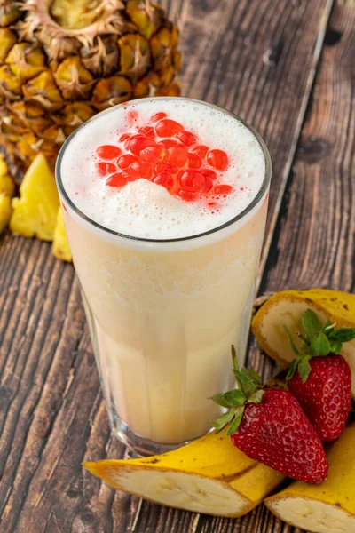 Banana, strawberry and pineapple smoothie on wooden table and bubble tea or boba tea balls on it