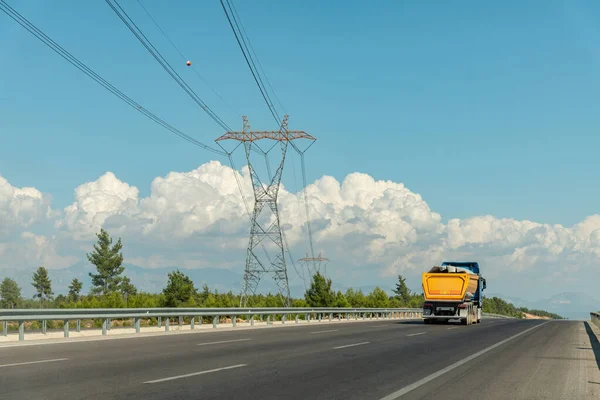 A truck going on a highway and a high-voltage power line on the side of the highway