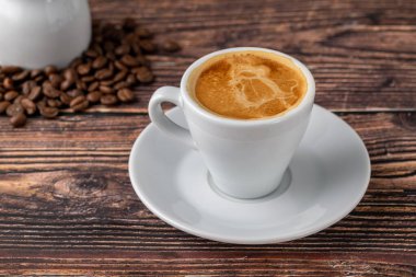 Beyaz bardakta espresso, yanında süt, ahşap masanın üstünde.