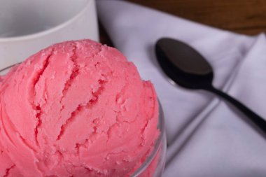 Arka planda bulanık elementlerle dolu cam bir kavanozda servis edilen çilek aromalı dondurma. Gurme yakın çekim fotoğrafçılık.
