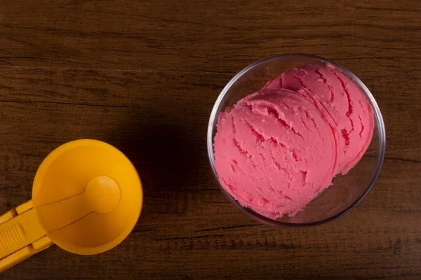 Tasty Strawberry flavored ice cream served in a glass bowl next to an ice cream scoop. Top view photography.