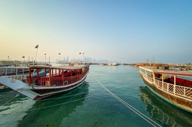 Cityscape and downtown skyscapers seen through traditional dhow boats at Corniche in Doha, Qatar against blue sky