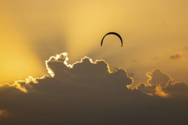 Gün batımında bulutlara ve turuncu gökyüzüne karşı uçan tek bir uçurtma.