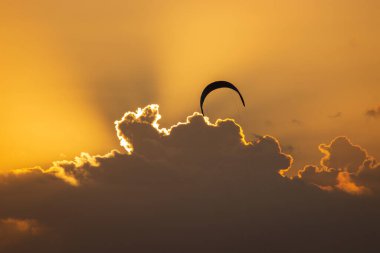 Gün batımında bulutlara ve turuncu gökyüzüne karşı uçan tek bir uçurtma.