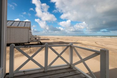 Hollanda, Kijkduin 'deki Kuzey Denizi sahilindeki kumsal kulübelerinin manzarası bulutlu mavi gökyüzüne karşı.