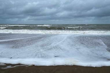 Hollanda 'da bulutlu gökyüzüne karşı sörf ve dalgalarla kumlu Kuzey Denizi plajı
