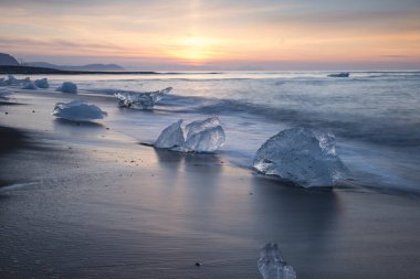 Elmas plajında güneş doğarken siyah kumların üzerinde buz bloğu