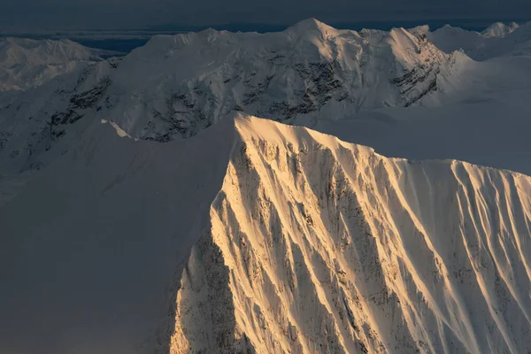 Sunset shines on snow covered peaks seen aerially in the Alaska Range of interior Alaska