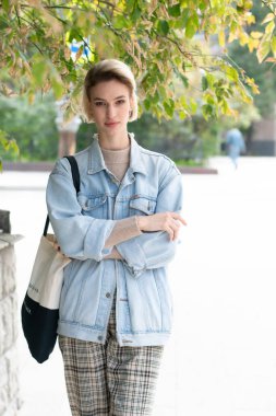 Genç ve güzel bir kadın dışarıda kot ceketle poz veriyor.