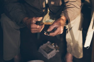 Yaşlı, bronzlaşmış erkek elleri elektrikli süpürgenin bozuk bir parçasını tutuyor.