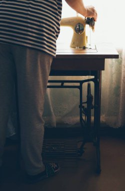 Kadın evde eski bir dikiş makinesine dikiş dikiyor.