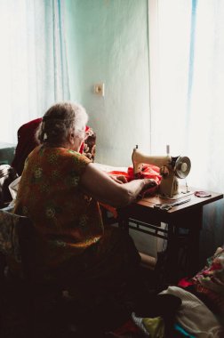 Kıvırcık saçlı yaşlı kadın dikiş makinesine dikiş dikiyor.