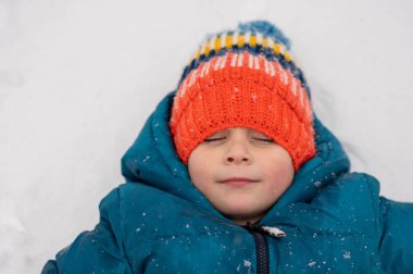 Little boy in knit cap making snow angels