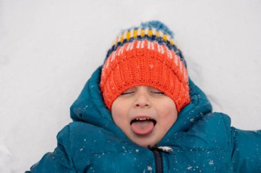 Little boy in knit cap catching snowflakes on his tongue