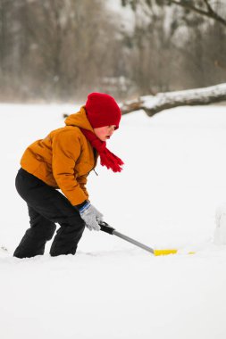 Parlak elbiseli bir çocuk karları kürekle temizliyor.