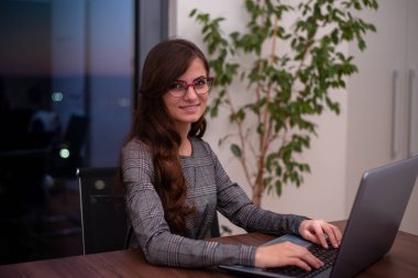 Genç bir kadın gülümsüyor ve laptopuyla çalışıyor.