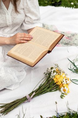 Papatyalı bir buket ve elinde açık bir kitap..