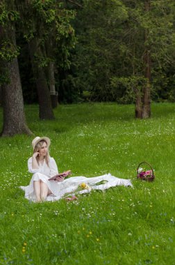 Ormanda battaniyenin üzerinde kitabı olan bir kız..