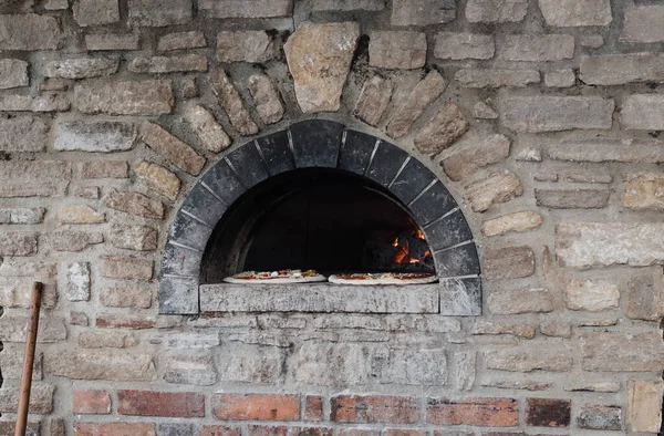 stone fired outdoor pizza oven with two pizzas ready to cook