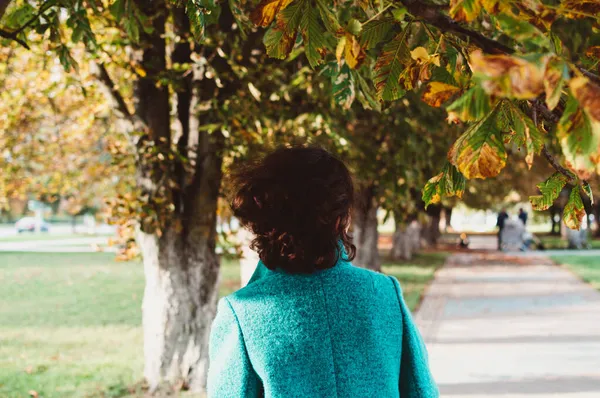 Sonbahar günü dalgalı siyah kıvırcık saçlı mavi paltolu kız.