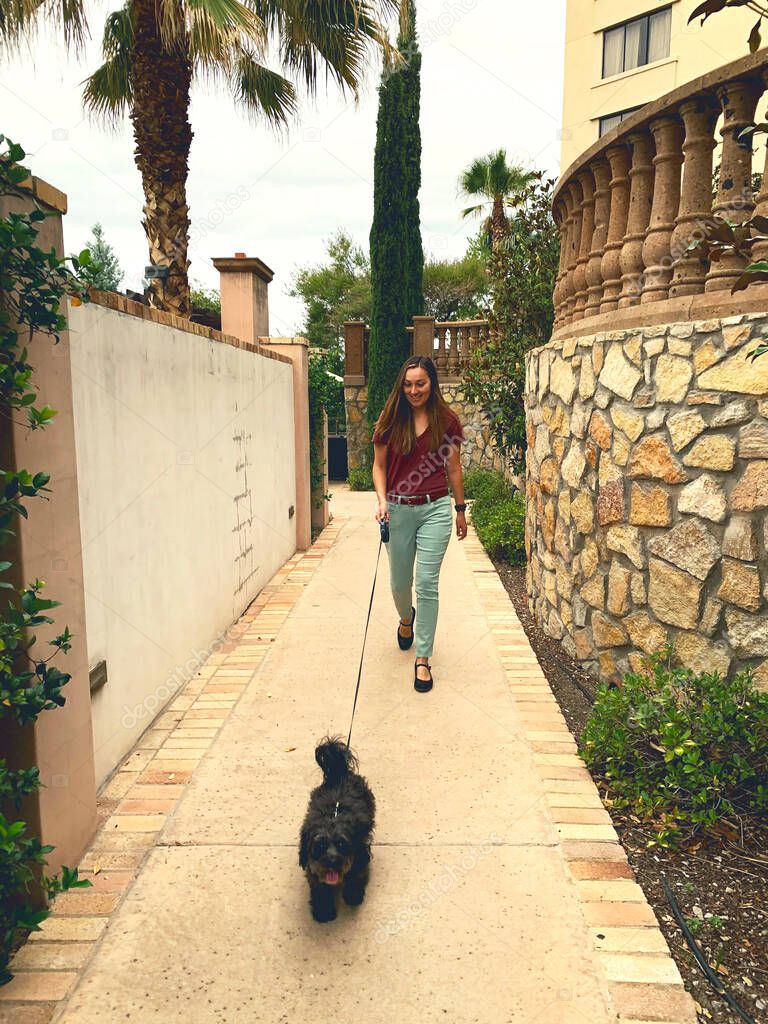 Latinx woman walks dog at Spanish-style hotel