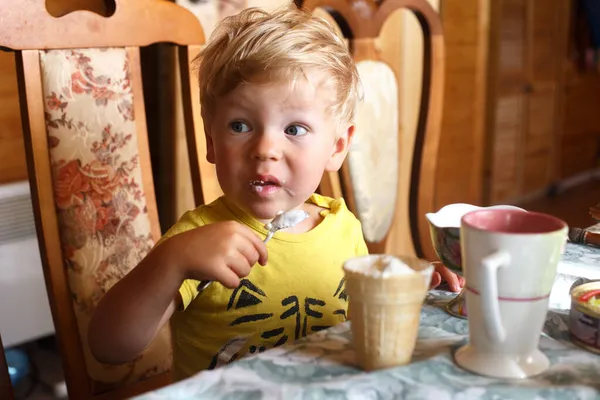 Ένα Ξανθό Αγόρι Κάθεται Στο Τραπέζι Και Τρώει Παγωτό Ένα — Φωτογραφία Αρχείου
