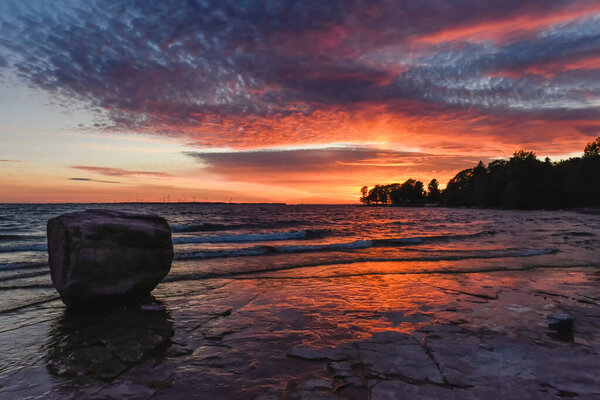 Beautiful colorful sunset on shoreline of lake with large rock.