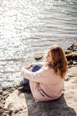 Bir kadın deniz kıyısında suyun arka planında oturur.