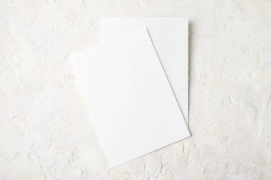 Işık taşı arka planında iki beyaz davetiye modeli, Minimalist model 5x7 oranı, A6, A5 'e benzer.