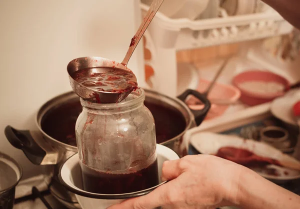用炉子上的一个大平底锅把热果酱放进玻璃瓶里 — 图库照片