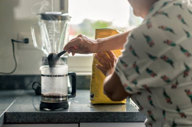 Latin büyükanne Fransız basınına topraklanmış kahve dolduruyor.