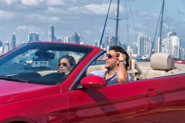 Latin çift arkada Panama City olan üstü açık kırmızı bir arabada gülümsüyor.