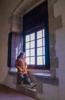 Klasik pencereden dışarı bakan konsantre ve rahat bir kız.