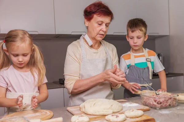 おばあちゃんは双子に伝統的な肉料理を作る方法を示しています — ストック写真