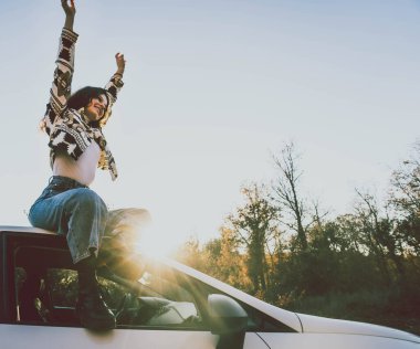 Gün batımında birçok ağacın ortasında bir arabanın tepesinde oturan bir kadın.