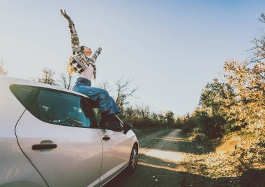 Gün batımında birçok ağacın ortasında bir arabanın tepesinde oturan bir kadın.