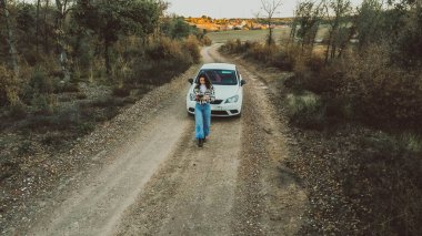 Ormanlar arasında beyaz bir arabanın önündeki kadın kuş bakışı.