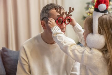 Kızı babasına Noel kıyafetleri giydirir.