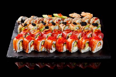 Avokado, kumkuat ve havyar ile süslenmiş somon, ton balığı ve yılan balıklı lezzetli uramaki, nigiri sushi ve gunkan maki seti siyah parlak arkaplanda servis edilir. Tipik Japon mutfağı.